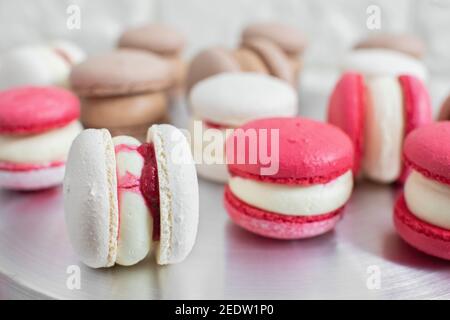Primo piano di colorati dessert di macaron al cioccolato bianco, rosso e caramello, ripieni di gustose ganache, sul tavolo in cucina leggera o dolciumi Foto Stock