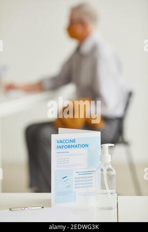 Immagine verticale del segno di vaccinazione di covid in clinica con l'uomo anziano che ottiene il vaccino in background, spazio di copia Foto Stock
