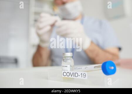 Primo piano di vaccino covid set sulla scrivania in clinica medica con medico offuscato in background, copia spazio Foto Stock