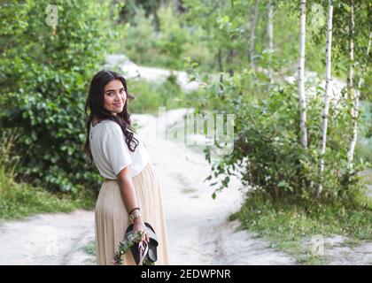 Bella giovane allegra donna incinta in fiori di corona sulla testa che tocca il ventre mentre cammina nel giardino dell'albero di primavera. Bellezza persone Lifestyle concetti Foto Stock