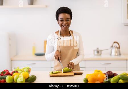 Happy African Housewife cucina taglio Zucchini verdure in cucina interno Foto Stock