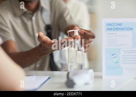 Primo piano di un uomo afroamericano irriconoscibile che usa l'igienizzatore a mano presso l'ufficio dei medici, spazio di copia Foto Stock