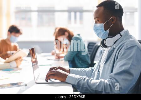 Persone internazionali che indossano maschere mediche utilizzando un computer portatile Foto Stock