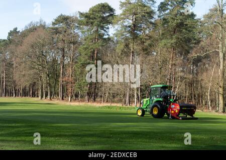 Groundsman falcia il verde con un trattore e un accessorio per falciatrice presso il golf club Aldershot Army, Hampshire, Regno Unito Foto Stock