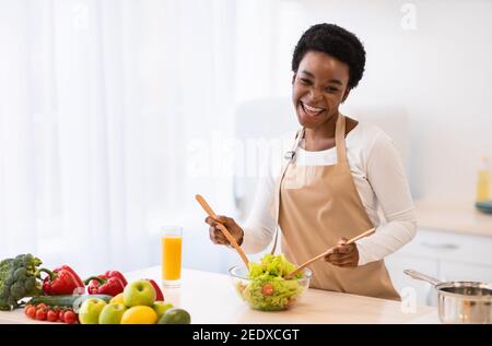 Cheerful African Housewife cucinare insalata di verdure in cucina a casa Foto Stock