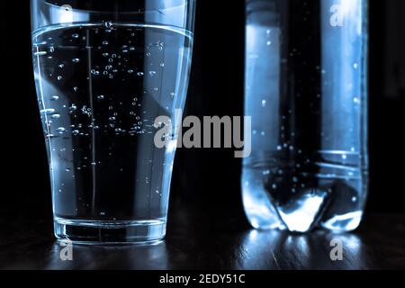 Un bicchiere di acqua frizzante o di soda. Acqua minerale frizzante in un bicchiere su sfondo scuro con una bottiglia d'acqua sullo sfondo. Sete. Bere Foto Stock