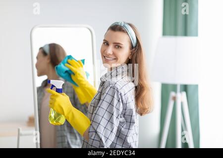 Giovane casalinga caucasica pulizia specchio, utilizzando spray detergente e straccio a casa. Concetto di servizio sanitario Foto Stock