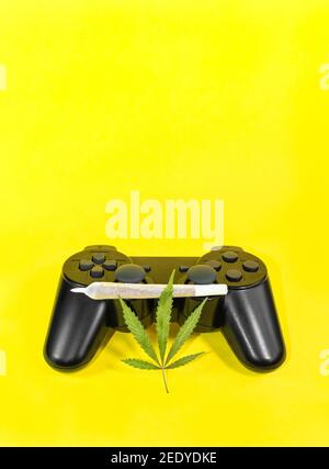 Video giochi e cannabis: Controller di gioco con foglia di marijuana e grande giunto di cannabis isolato su sfondo giallo con copy space top. Foto Stock