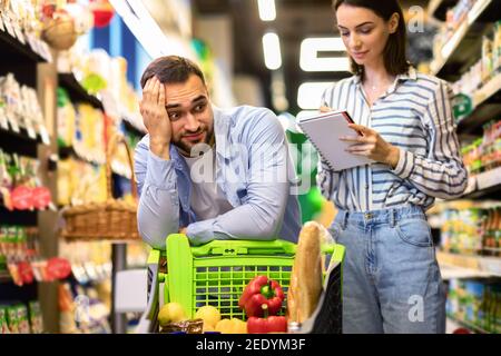 Divertente giovane coppia con la lista dei negozi nel supermercato Foto Stock