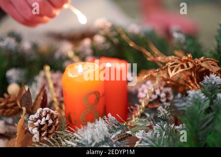 La mano di un uomo accende una candela rossa con il numero 8 circondato da rami artificiali di abete rosso con una partita Foto Stock