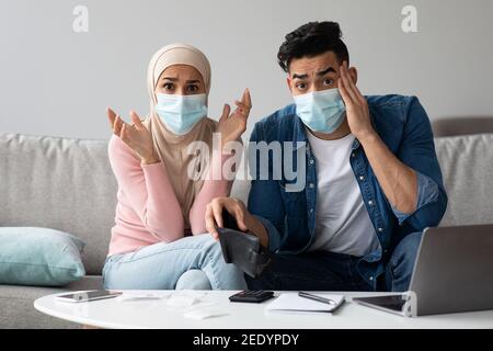 Coppia preoccupata in maschere facciali con portafoglio vuoto Foto Stock