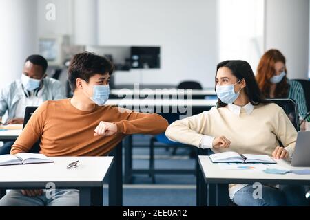 Diversi studenti che indossano maschere viso saluto e gomiti a urto Foto Stock