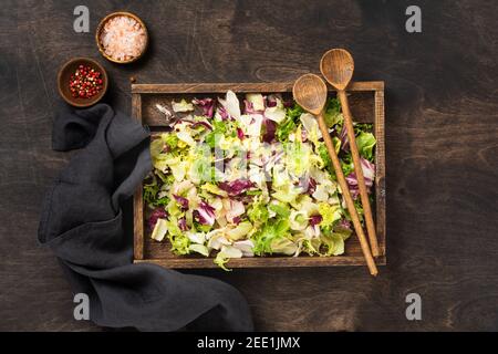 Mescolare le foglie fresche di rucola, lattuga, spinaci, barbabietole per insalata in scatola di legno su sfondo rustico di legno. Messa a fuoco selettiva. Foto Stock