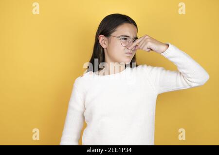 Bella bambina che indossa abiti casual odore qualcosa di stinoso e disgustoso, odore intollerabile, respiro trattenuto con le dita sul naso Foto Stock