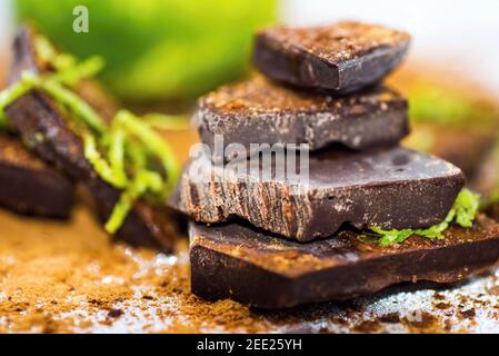 Spezzoni di cioccolato cosparsi di cannella e scorza di lime, frutti di lime sullo sfondo. Foto Stock