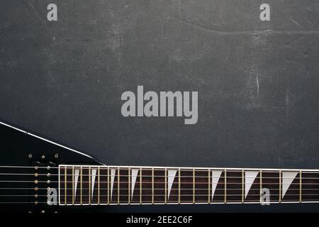 Vista dall'alto ripresa di una chitarra elettrica a V nera su sfondo scuro grunge con spazio di copia Foto Stock