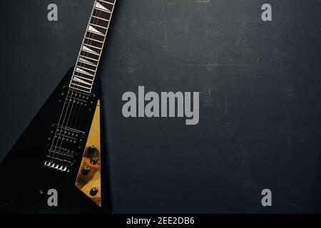 Vista dall'alto ripresa di una chitarra elettrica a V nera su sfondo scuro grunge con spazio di copia Foto Stock