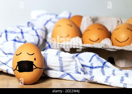 Uova di Pasqua creative con protezione del virus di Corona, uovo in una maschera nera in una quarantena. Uova di pollo diverse con sorriso su sfondo grigio. Disposizione piatta Foto Stock