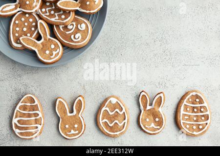 Biscotti decorati a Pasqua a forma di coniglietto e uova sono disposti in fila su uno sfondo grigio. Vista dall'alto Foto Stock