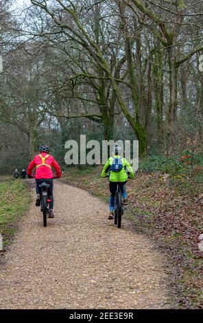 coppie anziane o di mezza età pedalando lungo un sentiero boscoso in inverno indossando abiti da ciclisti ad alta visibilità. Foto Stock