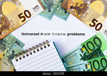 Foto in primo piano sul tema reddito base universale. Le parole Universal Basic Income Problems, sulla carta, circondato da banconote in euro e blocco note Foto Stock