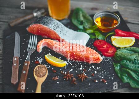 Filetto di salmone crudo e ingredienti per cucinare su sfondo scuro. Foto Stock