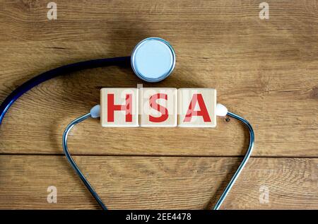 HSA, simbolo del conto di risparmio sulla salute. Cubetti di legno con le parole 'HSA, conto di risparmio di salute'. Stetoscopio. Sfondo di legno. Medico e HSA, salute sav Foto Stock