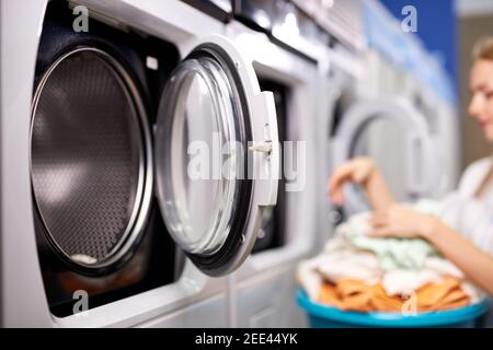 donna in casa di lavaggio smistamento vestiti puliti, facendo compiti domestici, donna tira fuori i vestiti dalla lavatrice, tenendo bacino. fuoco sulla lavatrice Foto Stock