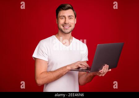 Ritratto fotografico di un giovane programmatore che lavora con il computer digitando testo sfondo di colore rosso brillante isolato e sorridente Foto Stock