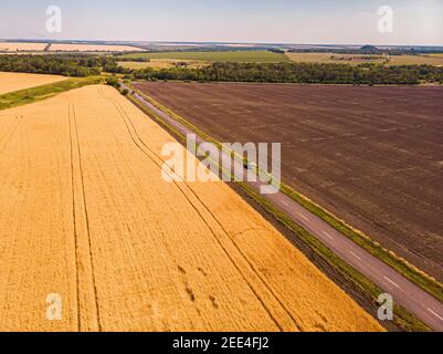 Veduta aerea di una stretta strada di campagna asfaltata grigia, che attraversa un paesaggio con campi e prati. Foto Stock