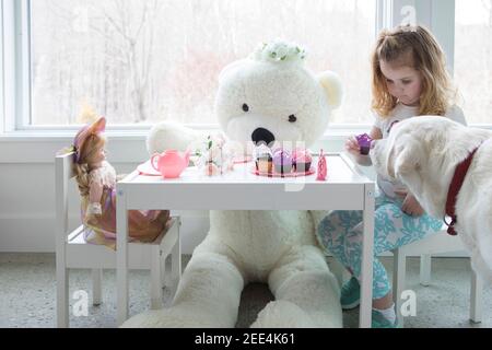 Una bambina che ha una festa del tè pretend con il suo cane e giocattoli. Foto Stock