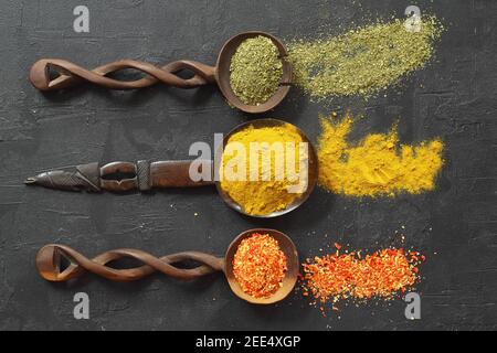 Diversi tipi di spezie su una pietra nera. Spezie orientali in cucchiai, peperoni rossi, curry in polvere, menta in polvere. Disposizione piatta, vista dall'alto. Foto Stock