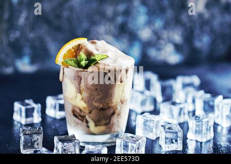 Gelato alla crema di soda arancio galleggianti in vetro decorato con pezzo di arancio, paillette e foglie alla menta, circondati da cubetti di ghiaccio sul retro del tavolo in pietra Foto Stock