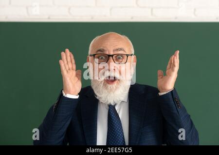 Vecchio volto sorpreso di divertente insegnante. Professore senior eccitato in lavagna. Foto Stock