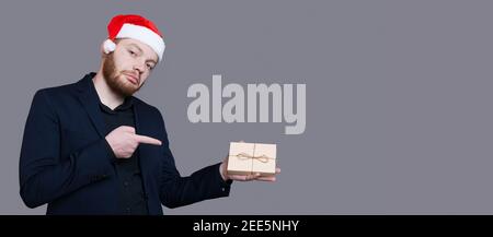 L'uomo bearded con il cappello di santa che indossa l'usura formale sta indicando al momento in mano che si posa su un grigio parete vicino a spazio libero Foto Stock