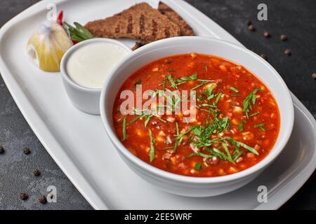 Borscht rosso su un piatto bianco con pane e panna acida, su fondo scuro Foto Stock