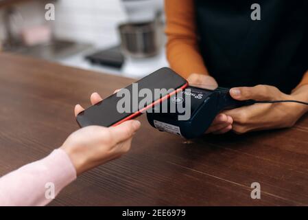 Concetto di pagamento senza contanti. Primo piano di cliente femmina tenere smartphone pagare per l'ordine utilizzando la tecnologia moderna, cameriera dare lettore di carta macchina per il cliente effettuare la transazione di pagamento utilizzando il cellulare Foto Stock