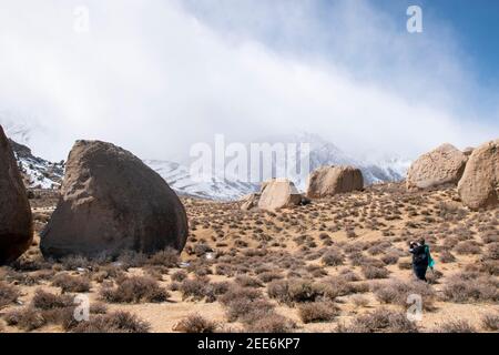 Una donna posa per le fotografie a Buttermilk Boulders vicino a Bishop, CA, USA, mentre il vento raccoglie la sua sciarpa. Foto Stock