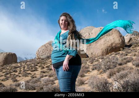 Una donna posa per le fotografie a Buttermilk Boulders vicino a Bishop, CA, USA, mentre il vento raccoglie la sua sciarpa. Foto Stock