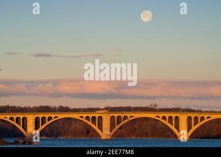 La luna piena tramonta alla luce del primo mattino su Key Bridge a Washington, DC. Foto Stock