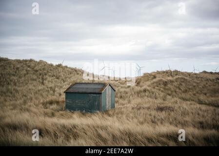 Capanna di pescatori di colore verde a South Gare, Redcar, Inghilterra, vicino a Paddy's Hole, con Teeside Wind Farm sullo sfondo offshore. Foto Stock