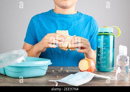 Le scuole pubbliche stanno riaprendo negli Stati Uniti dopo l'educazione virtuale a causa della pandemia di COVID 19. Un allievo caucasico della scuola elementare sta mangiando il suo panino al Foto Stock