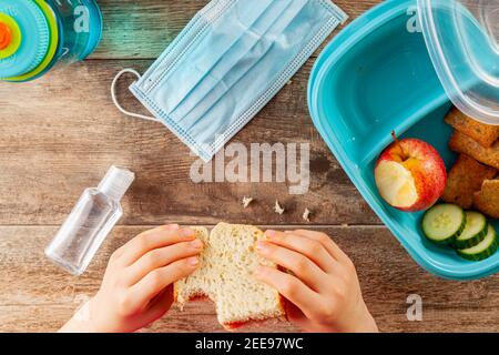 Immagine piatta con pranzo a scuola durante la riapertura graduale dopo la chiusura pandemica del COVID-19. Snack in contenitori e acqua Foto Stock