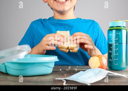 Le scuole pubbliche stanno riaprendo negli Stati Uniti dopo l'educazione virtuale a causa della pandemia di COVID 19. Un allievo caucasico della scuola elementare sta mangiando il suo panino al Foto Stock