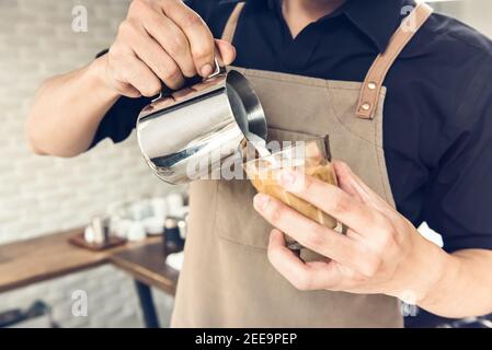 Barista professionista che versa il latte in cottura a vapore in una tazza di caffè e prepara il latte arte nel caffè Foto Stock