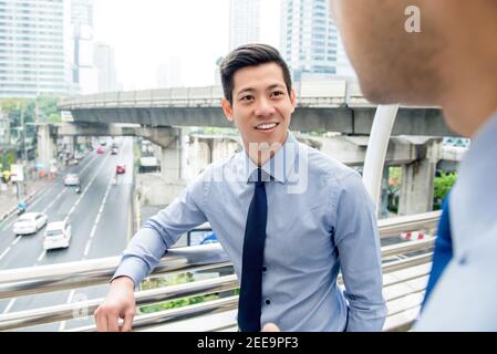 Sorridente bell'uomo d'affari cinese asiatico che parla con un collega all'aperto la città Foto Stock