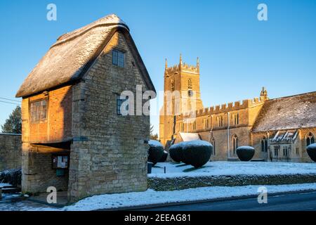 Chiesa di San Pietro e San Paolo e porta di Lych nella neve di gennaio appena dopo l'alba. Long Compton, Warwickshire, Inghilterra Foto Stock