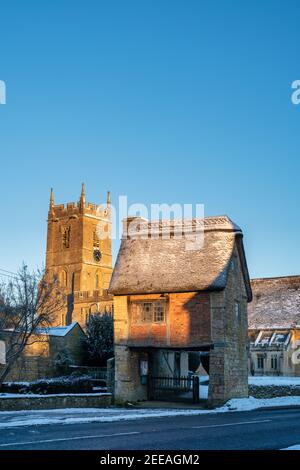 Chiesa di San Pietro e San Paolo e porta di Lych nella neve di gennaio appena dopo l'alba. Long Compton, Warwickshire, Inghilterra Foto Stock