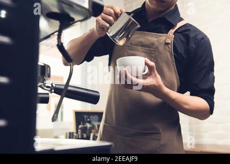 Barista professionista che versa il latte in cottura a vapore in una tazza di caffè e prepara il latte arte nel caffè Foto Stock