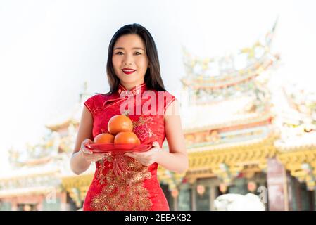 Bella donna asiatica in tradizionale abito qipao rosso adorando dio Con arance come offerta durante la stagione cinese di nuovo anno nel tempio Foto Stock